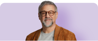 Man smiling in brown suede jacket and grey t-shirt with purple background