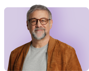 Man smiling in brown suede jacket and grey t-shirt with purple background